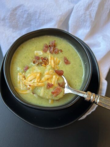 broccoli soup in black bowl on black plate with spoon