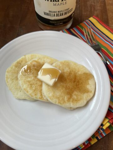 gluten free pancakes butter and syrup on a white plate with fork and striped napkin in background