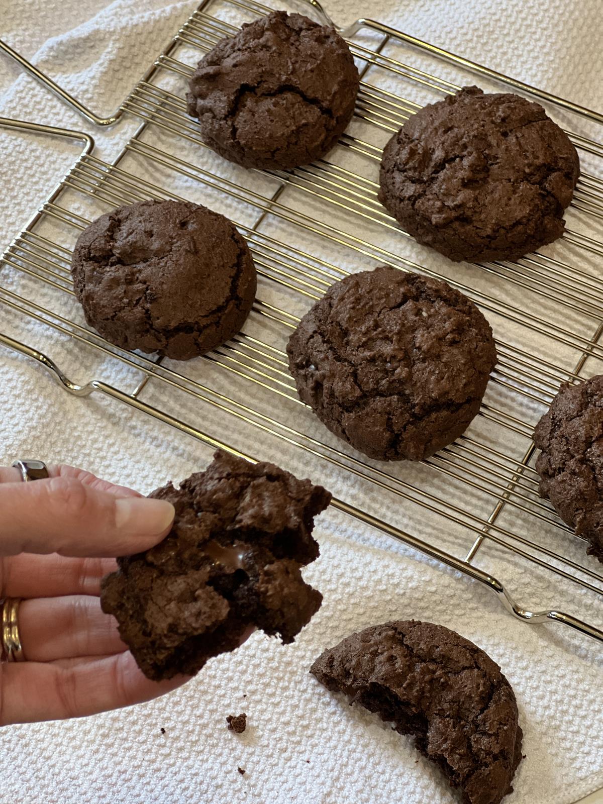 hand holding gluten free crumble brownie cookie with rack of cookies in background