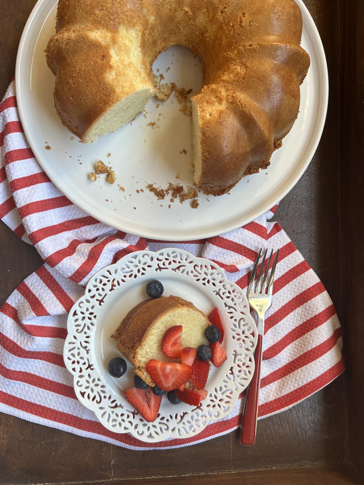 cold oven poundcake on white platter with piece of cake on plate with berries