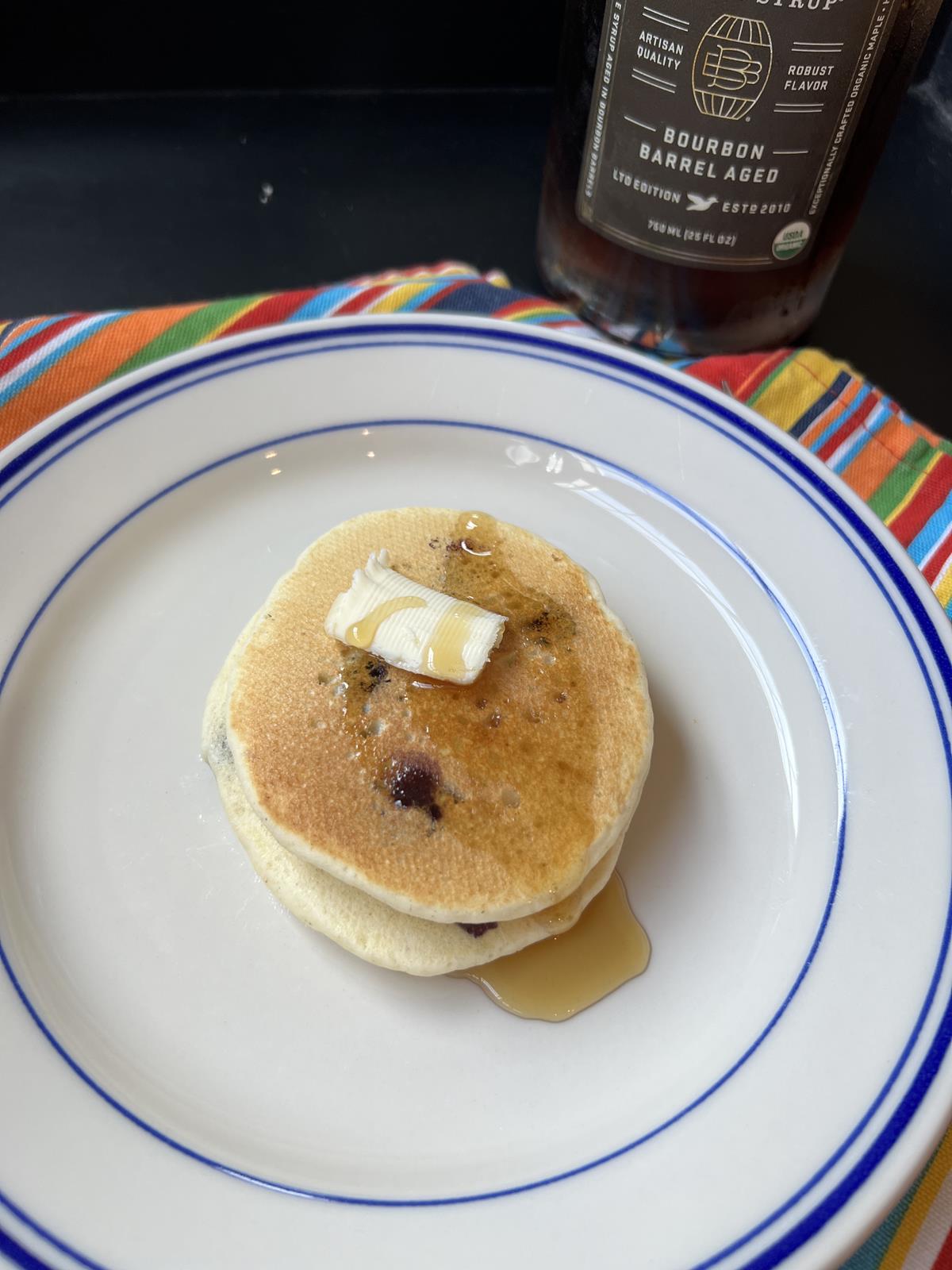 Martha Stewart's Blueberry Pancakes with butter and syrup on white and blue plate with striped napkin in background