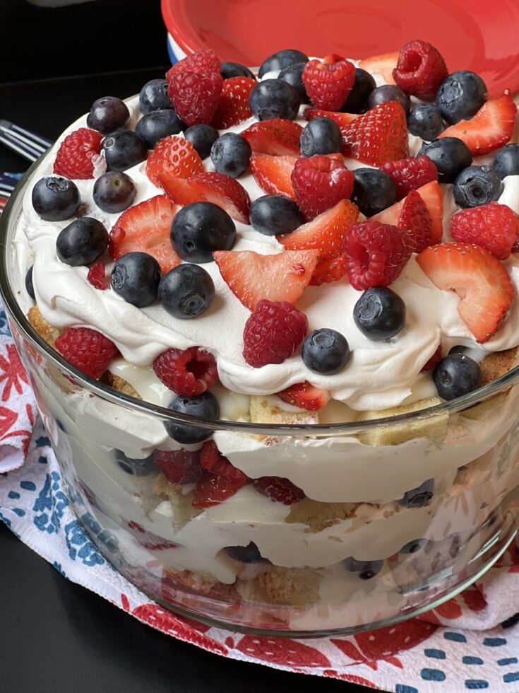 white chocolate berry trifle in glass bowl with red white and blue plates in background