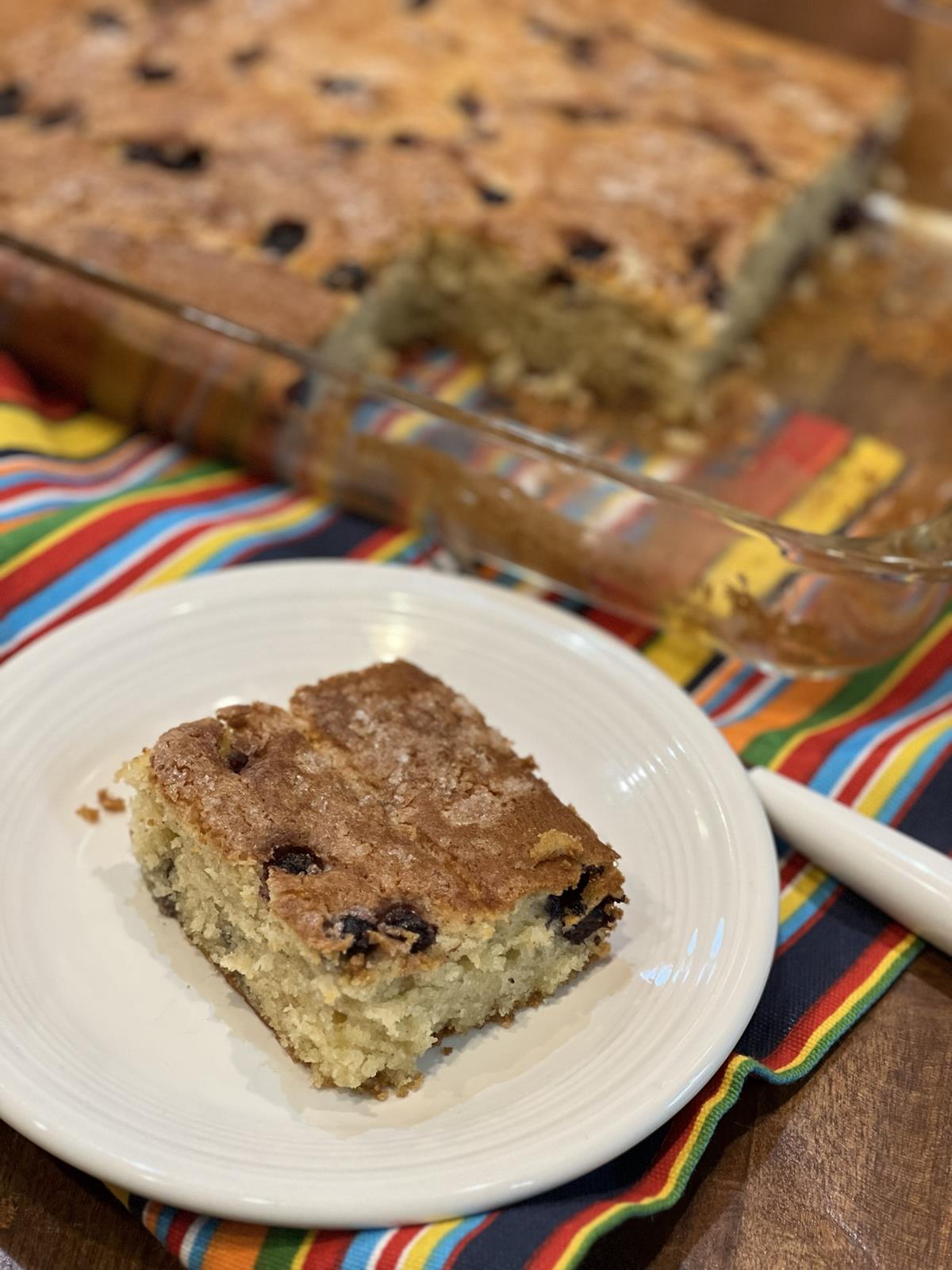 blueberry coffee cake on white plate with cake in glass pan in background