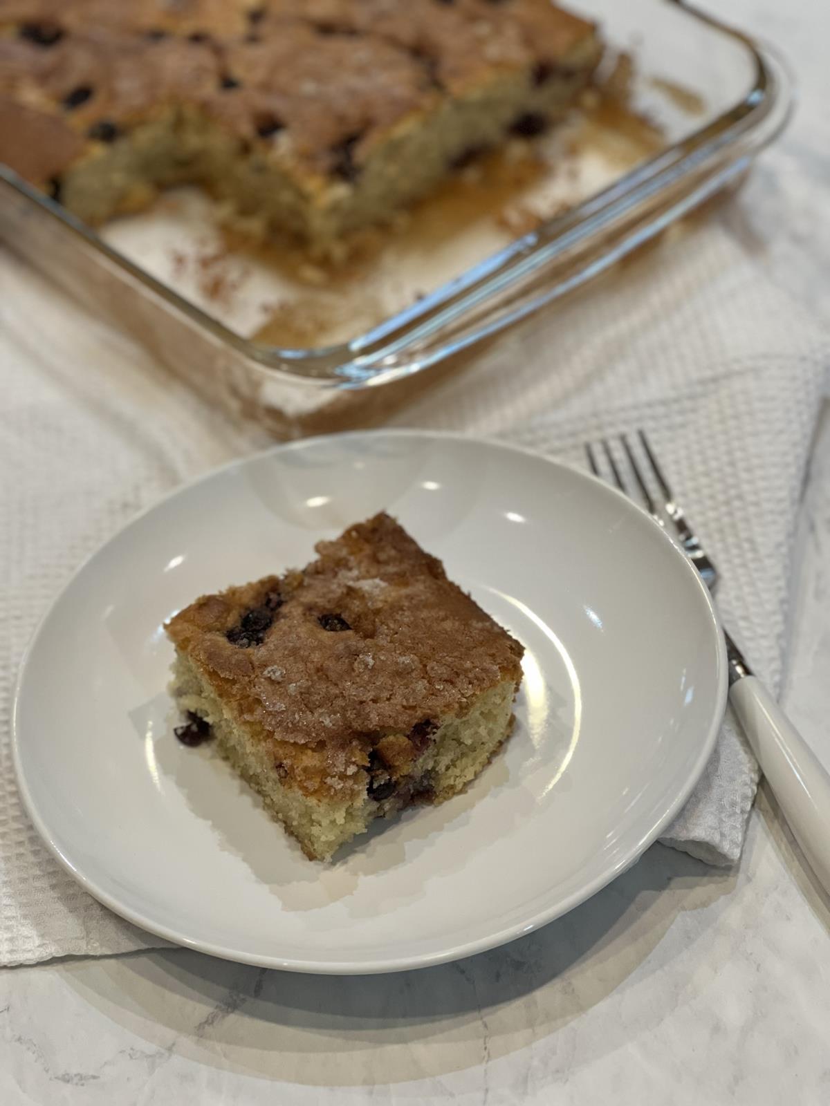 gluten free blueberry coffee cake on white plate with white fork with cake in glass pan in background