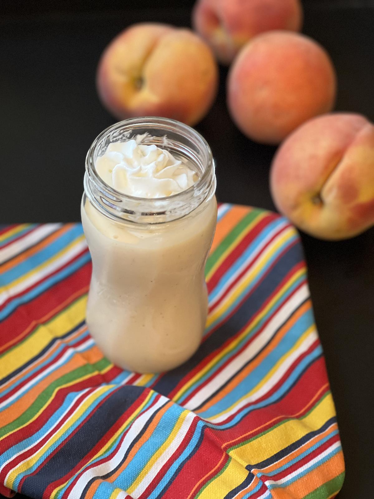 gluten free peach milkshake with whipping cream in glass jar with peaches in background