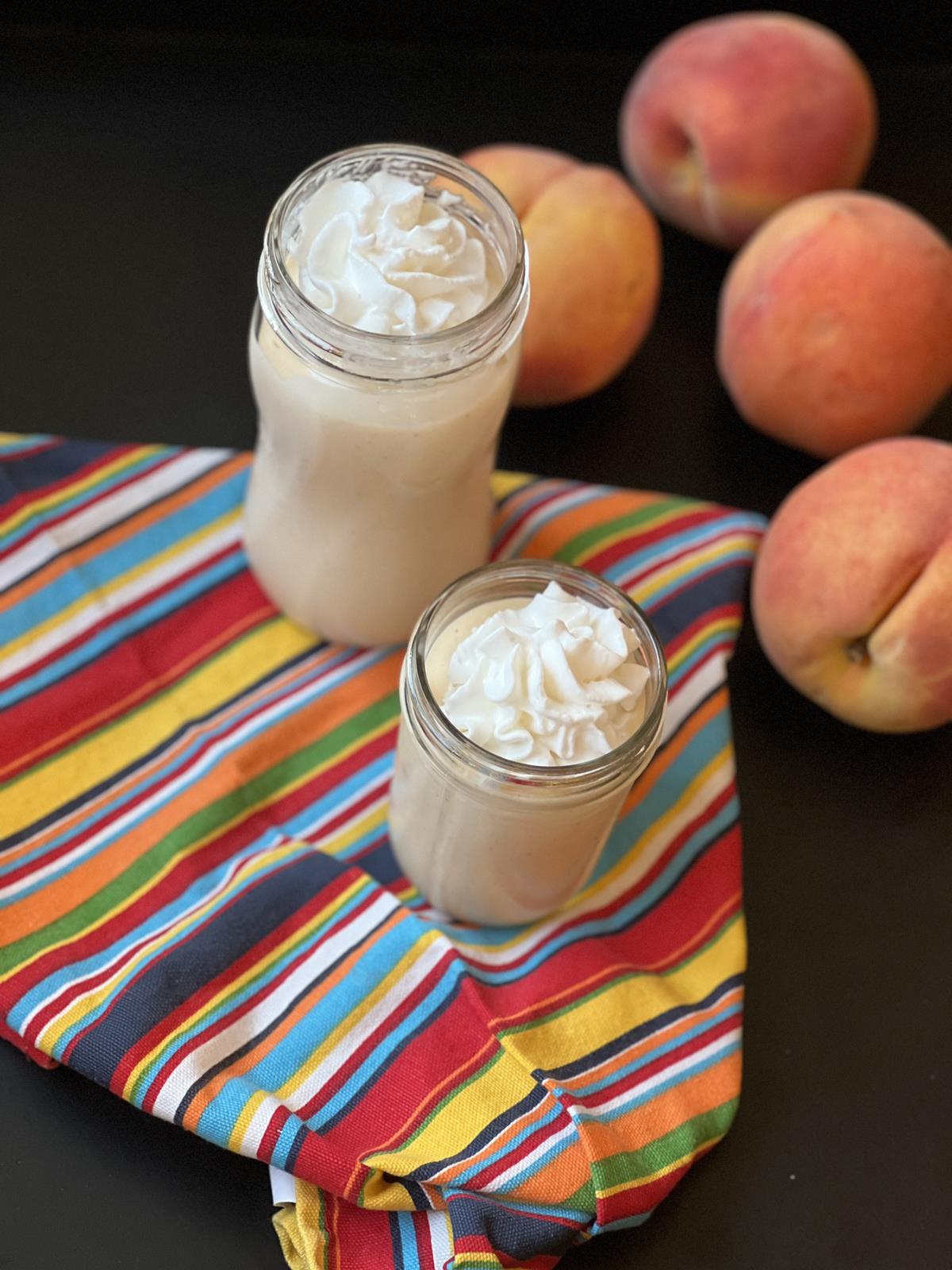 peach milkshakes in glass cups on striped napkins with peaches in background