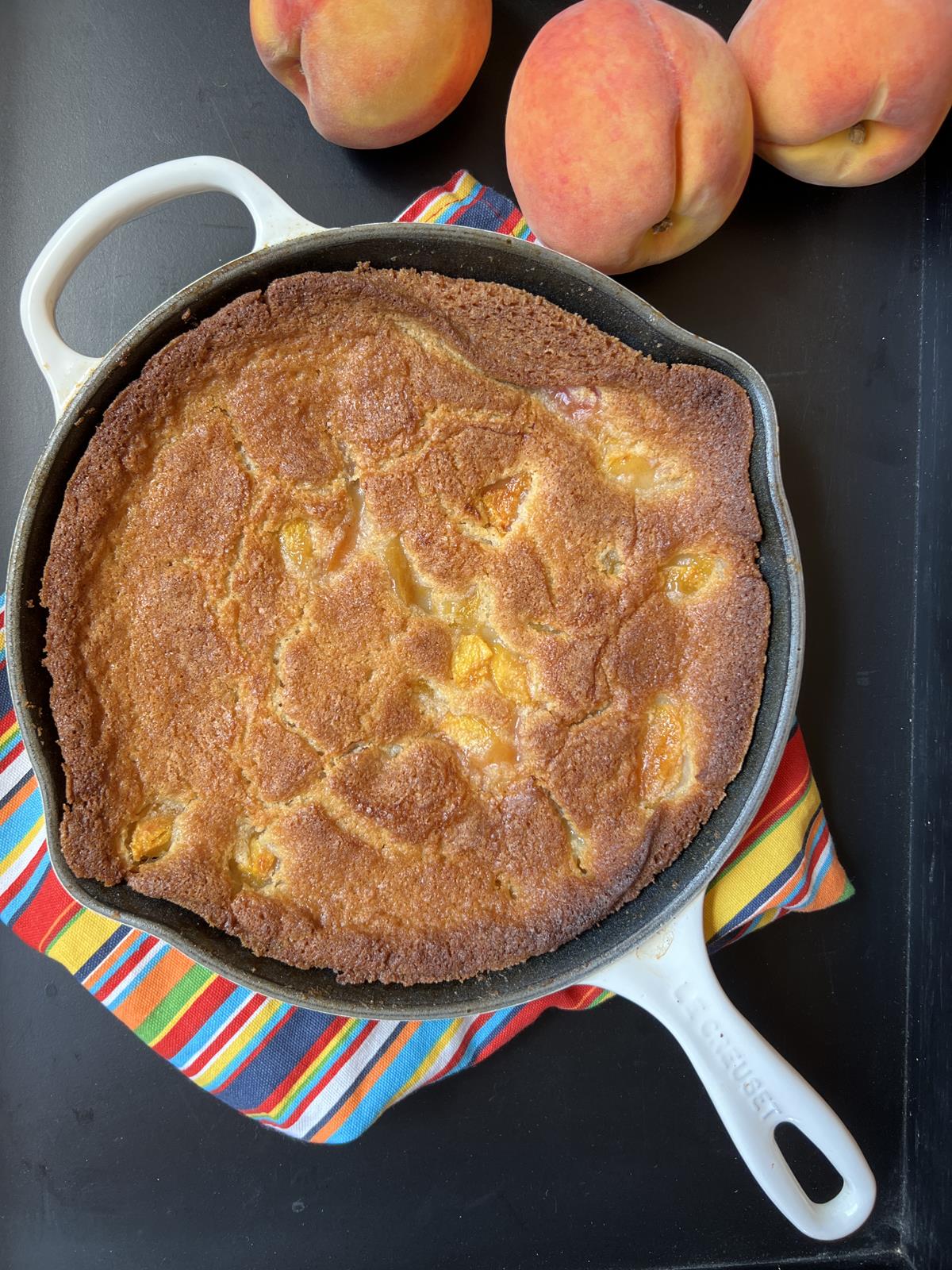 Martha Stewart Peach Buckle in cast iron pan with peaches in background