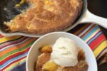 Martha Stewart Peach Buckle with ice cream in white bowl with cobbler in cast iron pan