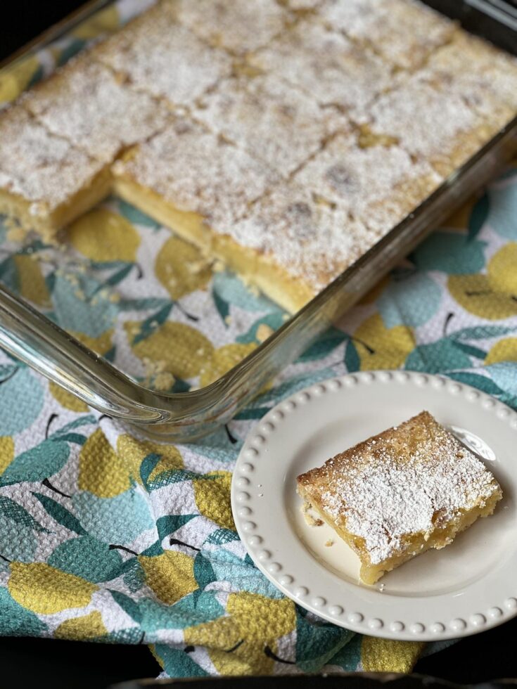 lemon bar on white plate on napkin with lemons printed on it.