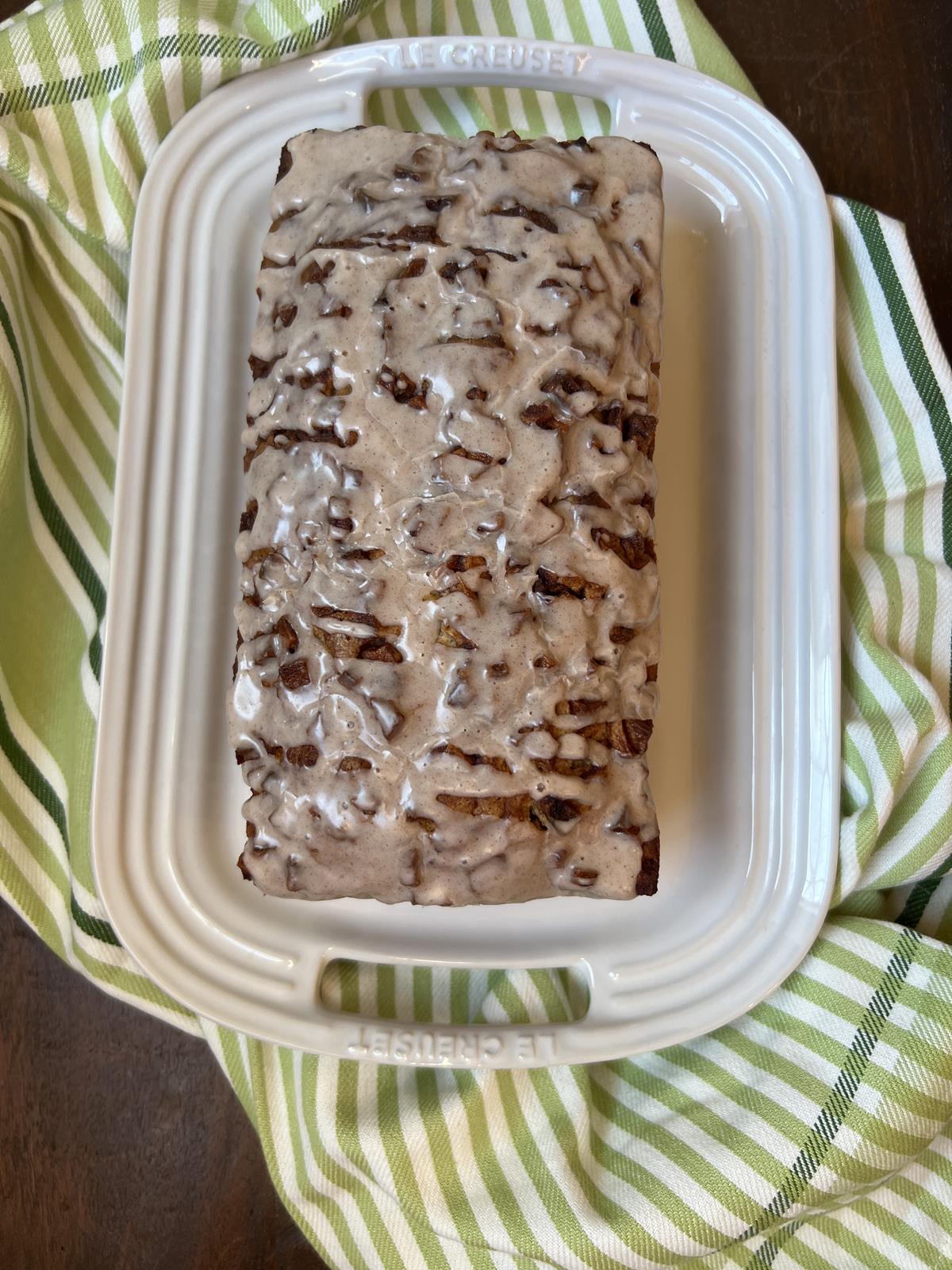 loaf of gluten free apple fritter bread on white platter with green and white striped napkin