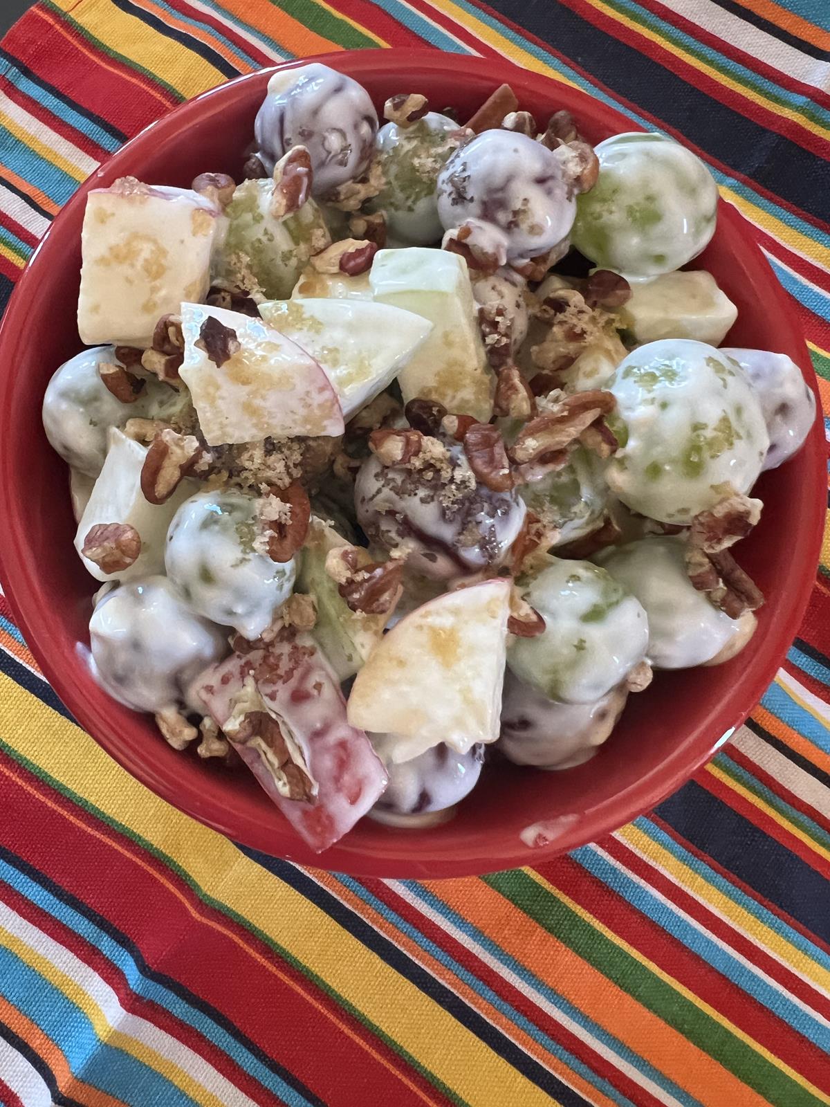 grapes, apples, and pecan fruit salad in red bowl on striped napkin