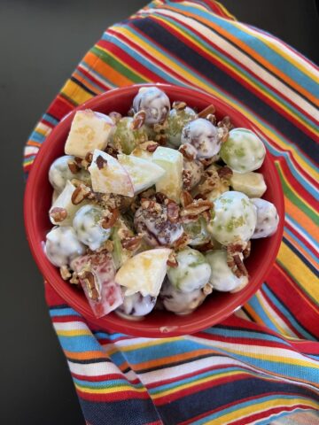 grapes, apples, and pecans fruit salad in red bowl on striped napkin