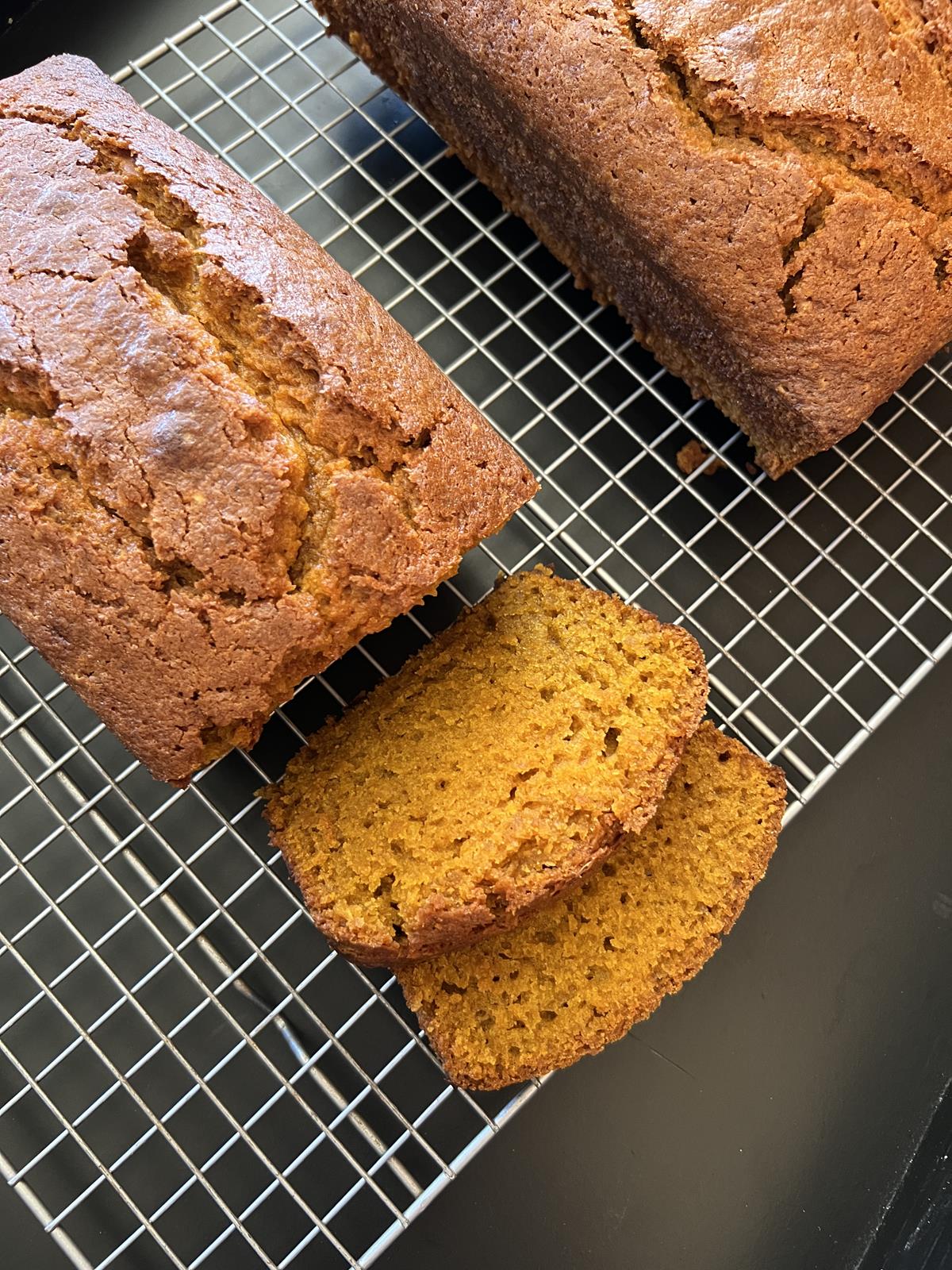 Loaf of pumpkin bread with two slices on cooling rack