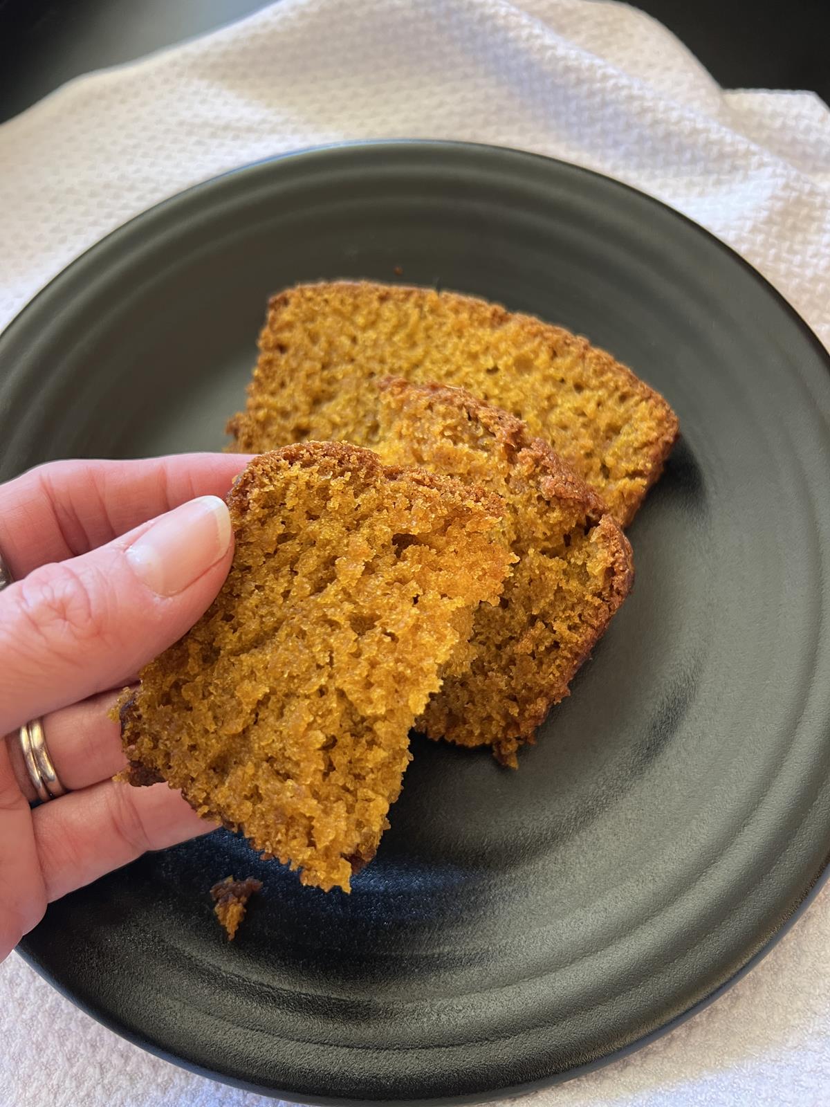 hand holding slice of pumpkin bread with black plate and white napkin in background