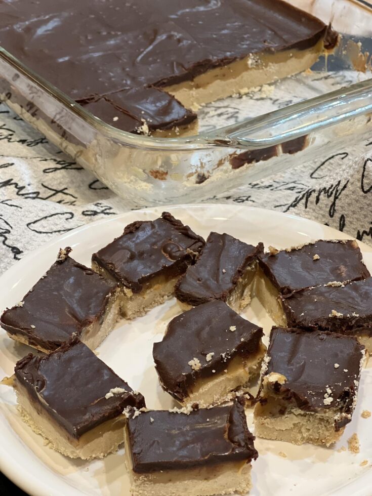 Chocolate Caramel Shortbread Bars Recipe on white plate with glass pan of bars in background