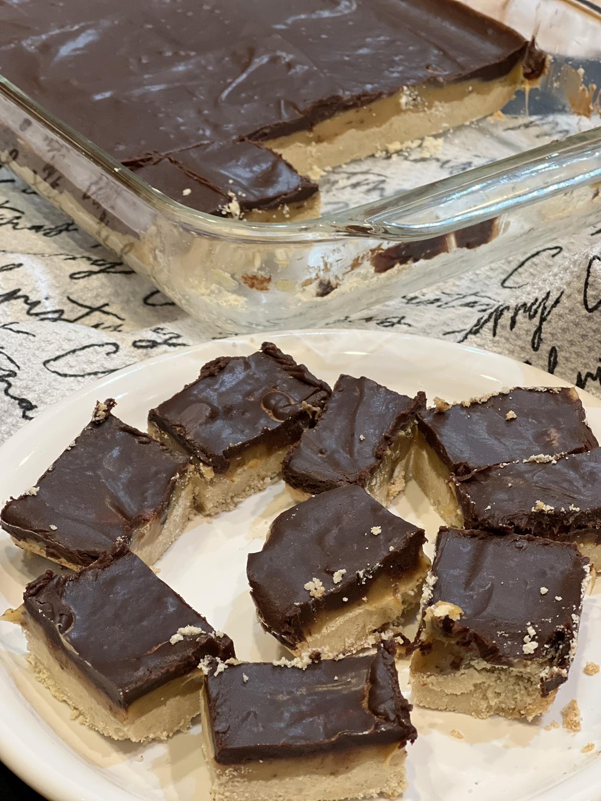 Chocolate Caramel Shortbread Bars Recipe on white plate with glass pan of bars in background