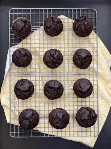 chocolate muffins on a wire cooling rack with yellow towel underneath