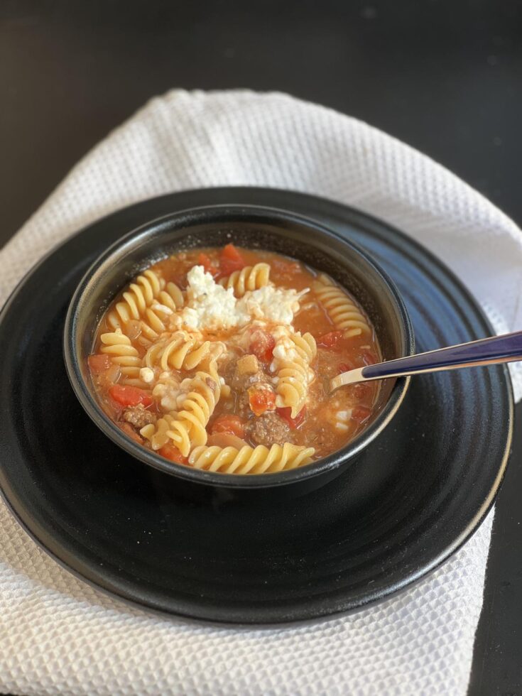 lasagna soup with cottage cheese in black bowl on black plate with spoon and white napkin