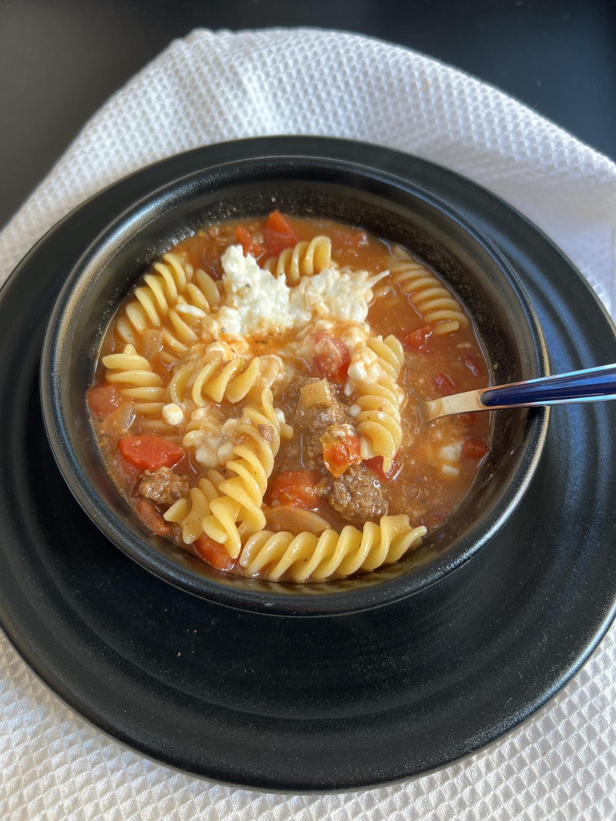 lasagna soup with cottage cheese in black bowl on black plate with spoon and white napkin