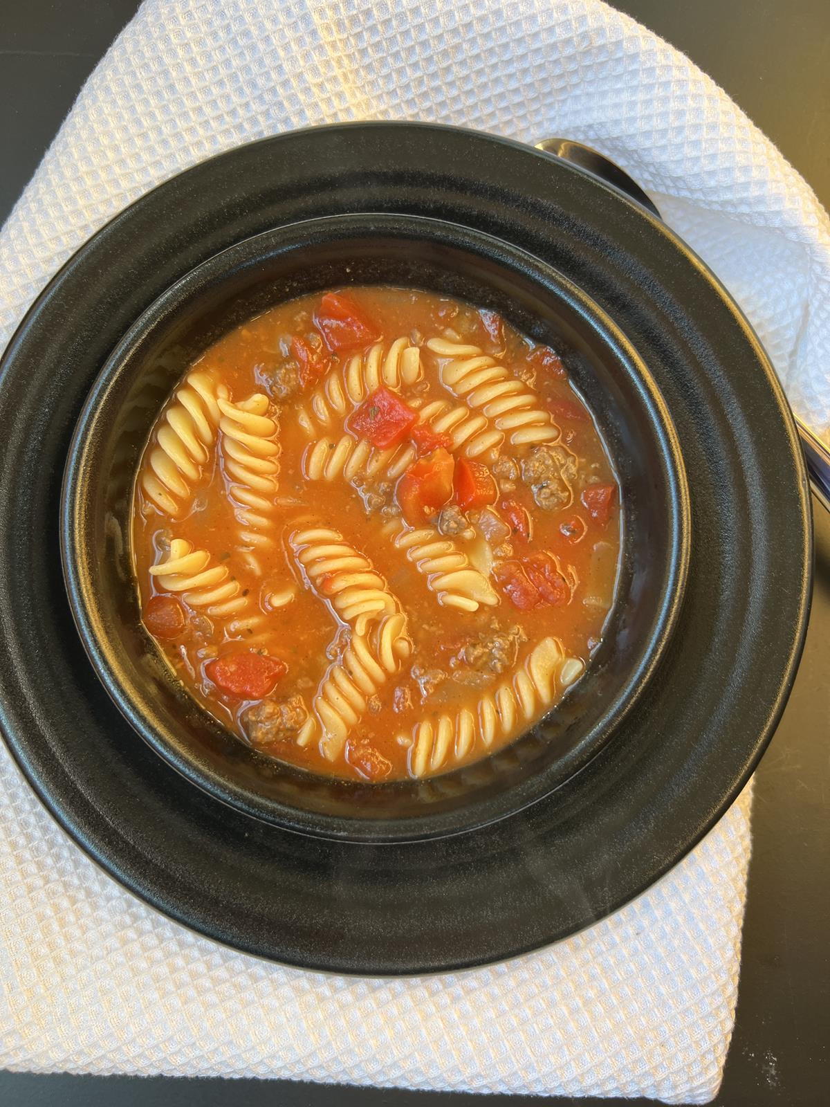 lasagna soup with cottage cheese in black bowl on black plate on white napkin