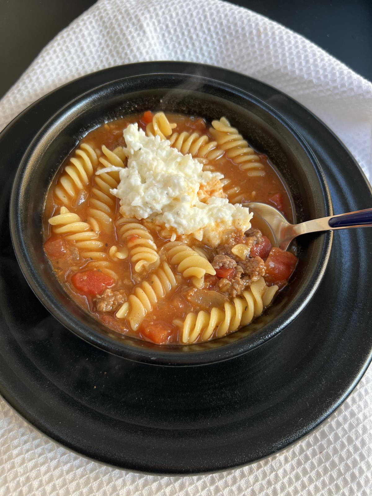 lasagna soup with cottage cheese in black bowl on black plate with spoon and white napkin