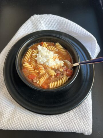 lasagna soup with cottage cheese in black bowl on black plate with spoon and white napkin