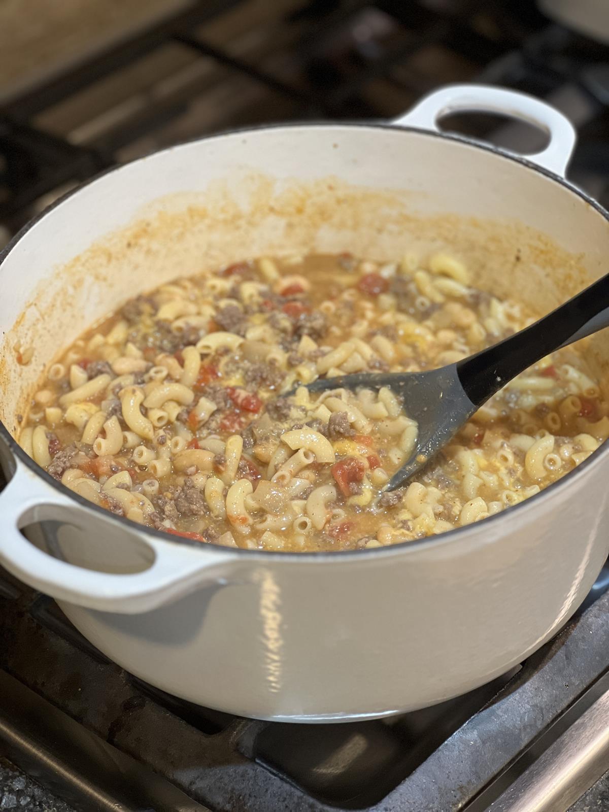 Mac and Cheese Chili in white cast iron pan with spoon on stove