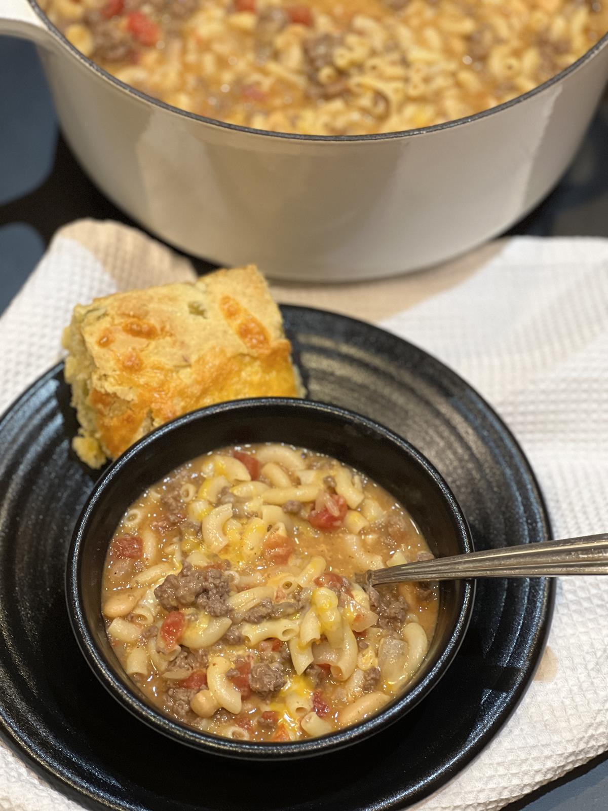 mac and cheese chilil soup in bowl on a plate with cornbread next to it and pan of soup in background