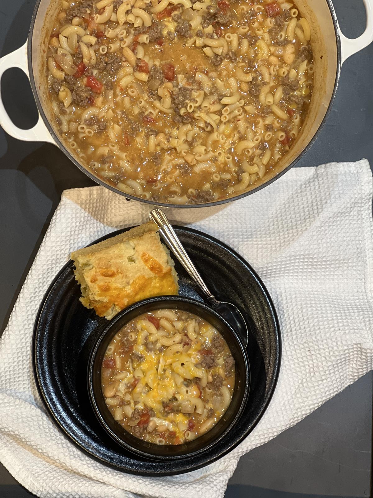 chili wit pasta in pan with a bowl of soup on a plate with cornbread and a spoon