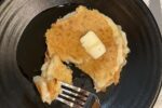 cottage cheese pancakse with butter and syrup on black plate with red fork and white napkin