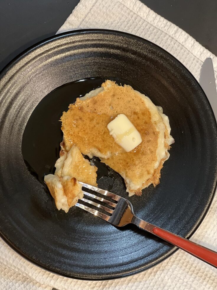 cottage cheese pancakse with butter and syrup on black plate with red fork and white napkin