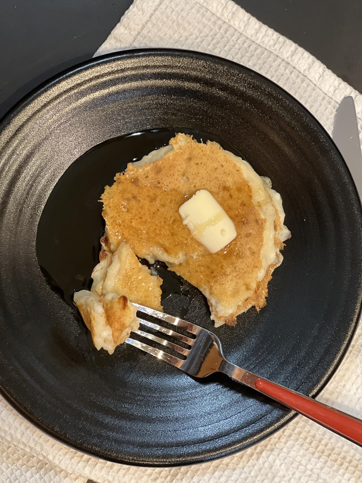 cottage cheese pancakse with butter and syrup on black plate with red fork and white napkin