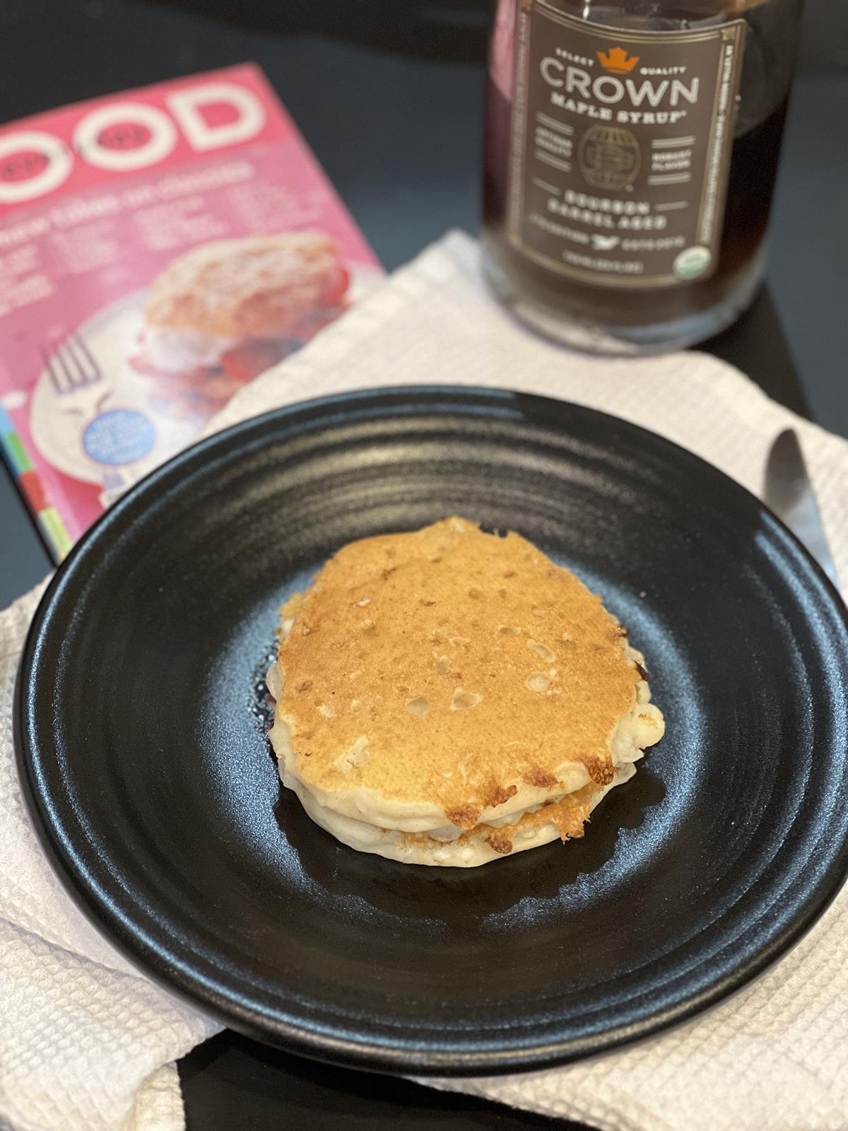 cottage cheese pancakse on black plate on white napkin with maple syrup and magazine in background