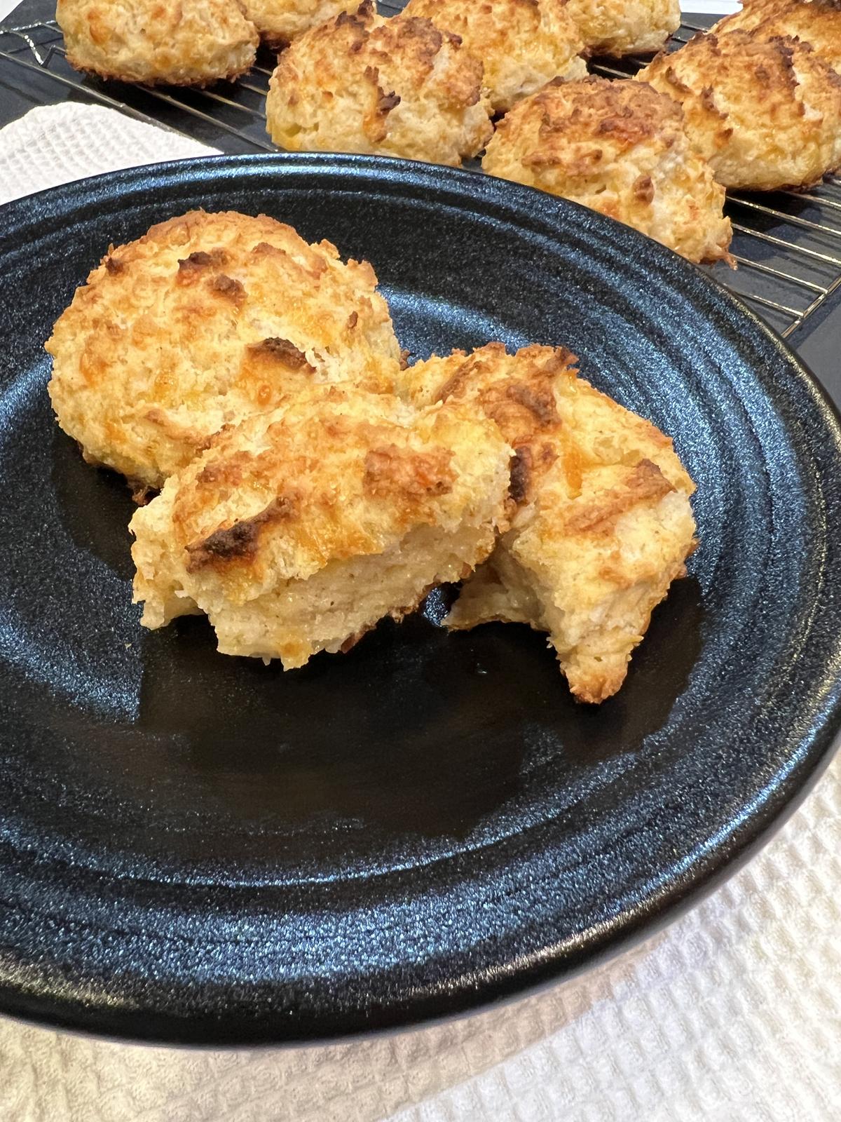 cheddar biscuits on black plate on white napkin with biscuits on cooking rack in background