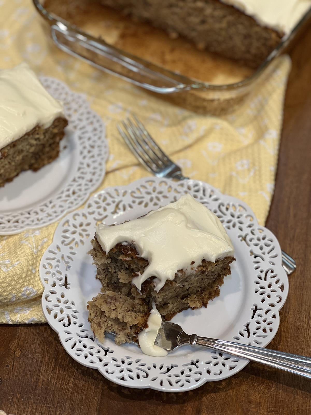 banana cake with frosting on white plate with fork on yellow and white napkin