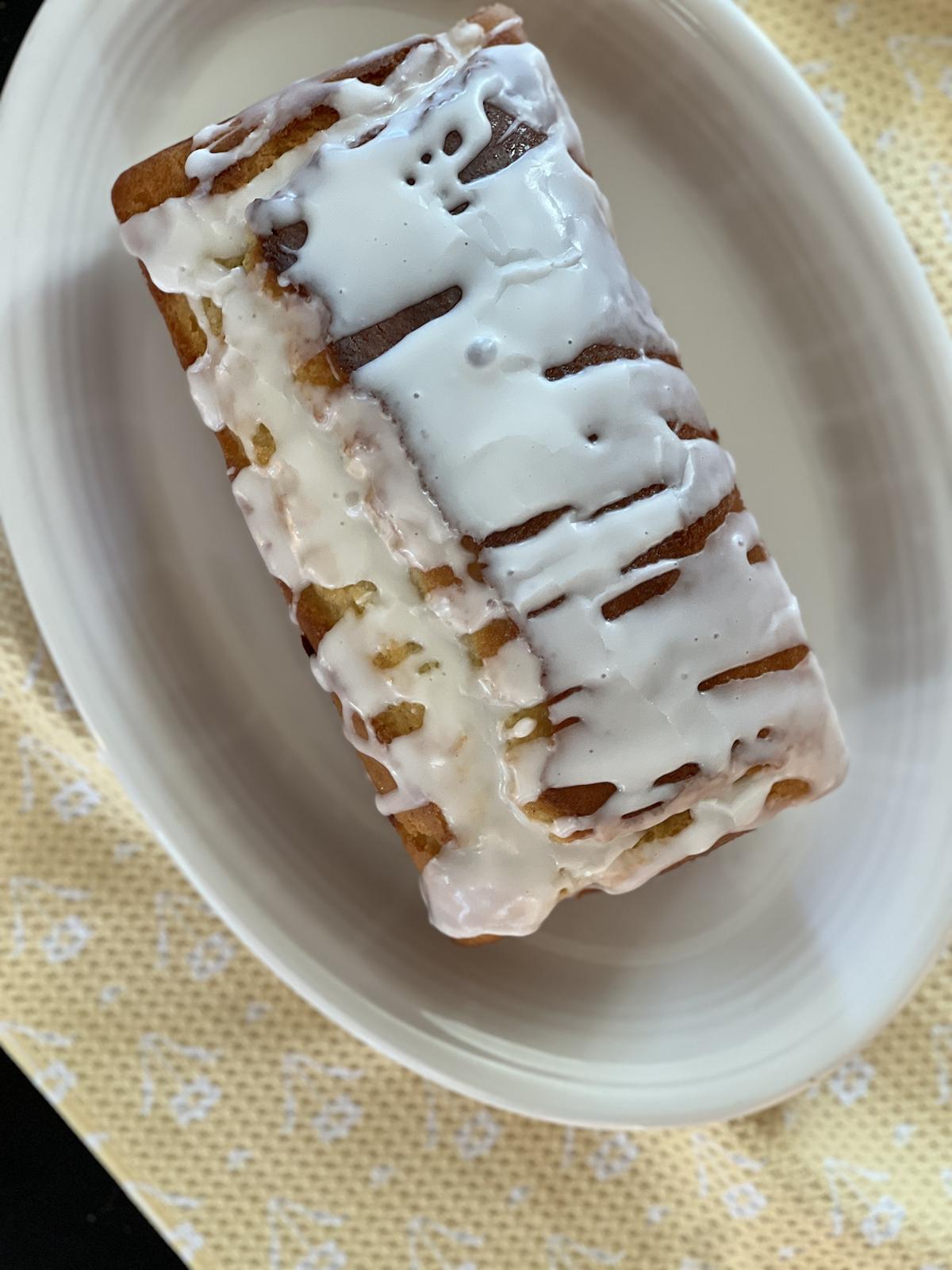 lemon yogurt cake with glaze on white platter on yellow napkin