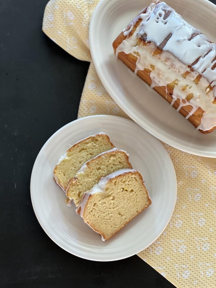 lemon yogurt cake on white plate with loaf cake on white platter on yellow napkin