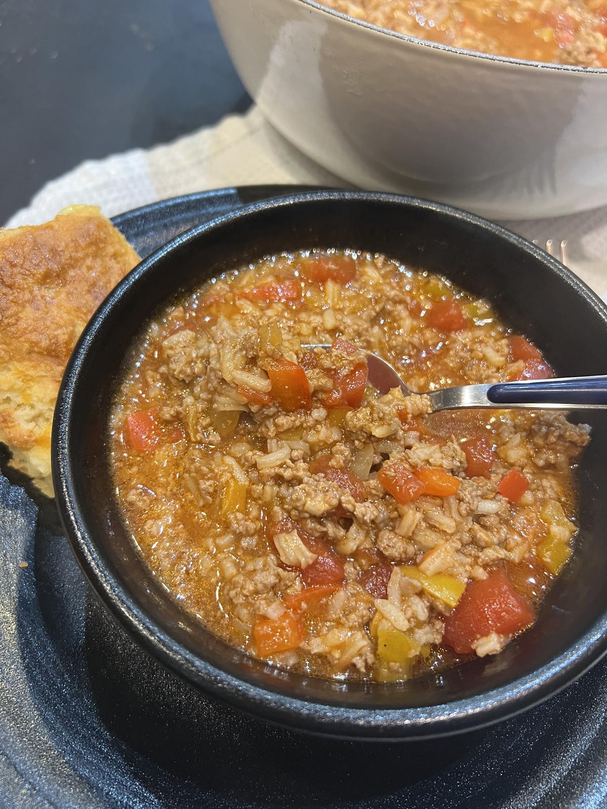 bowl of stuffed pepper soup with spoon and white pot of soup in background