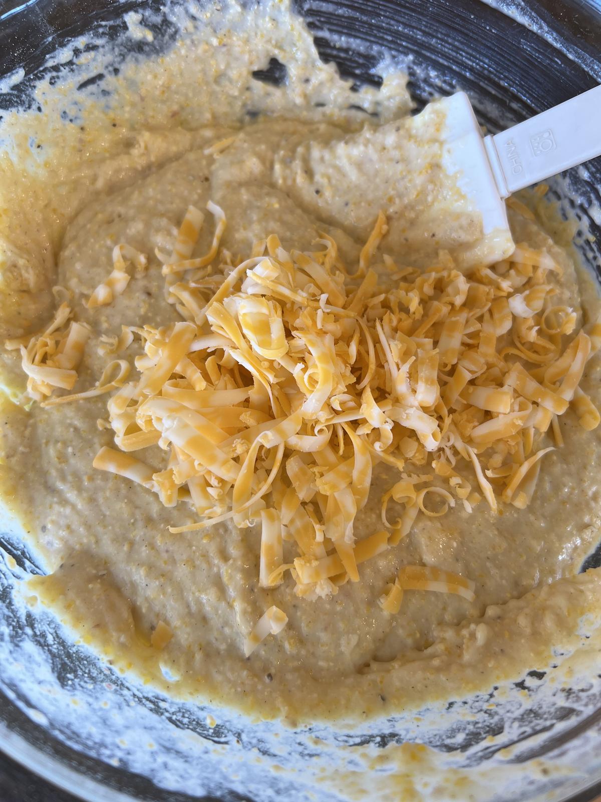 cornbread batter with cheese in glass bowl with spatula stirring