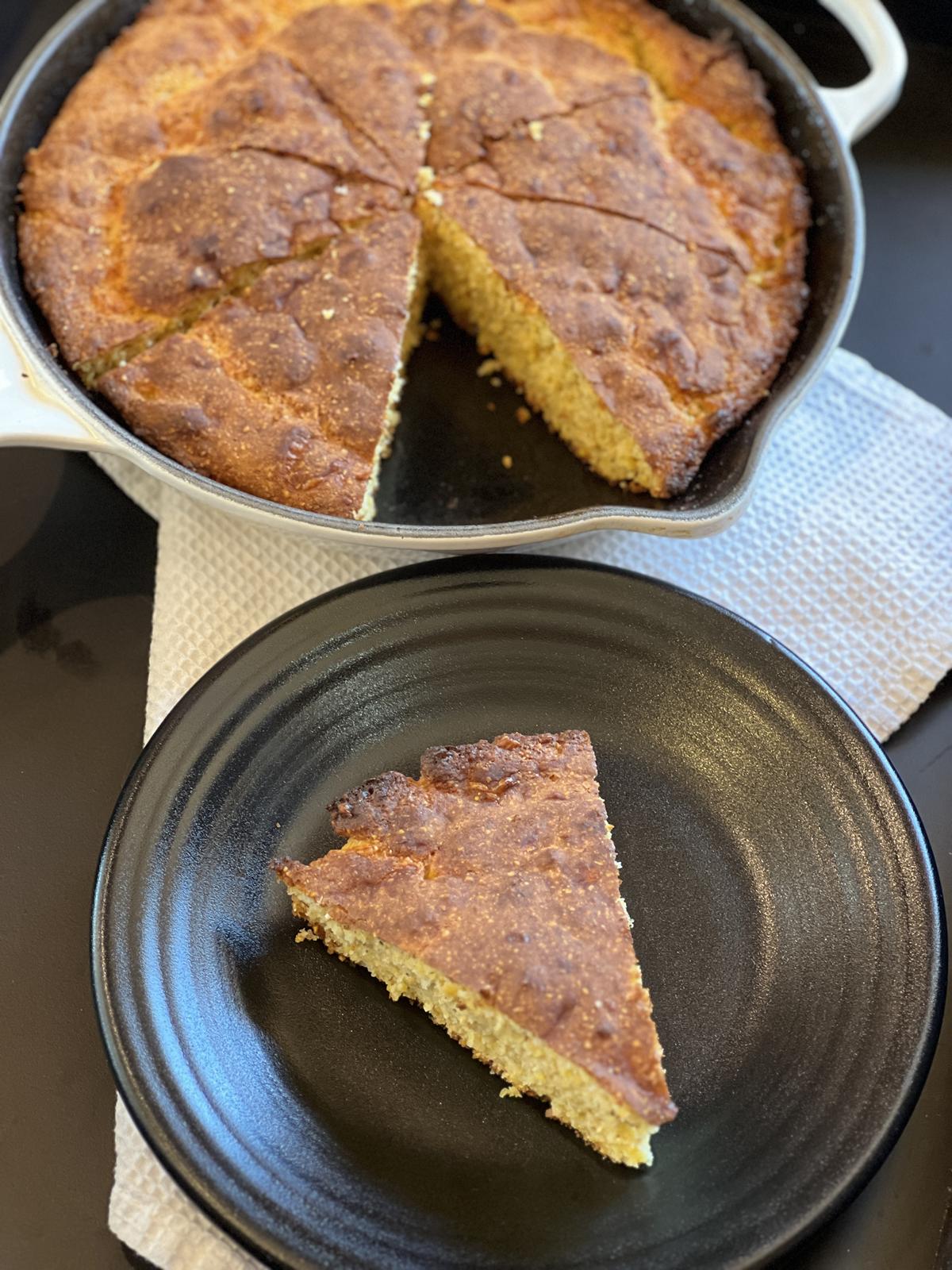 cornbread on black plate with skillet of cornbread in background